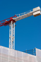 Construction site with red and white crane and a scaffolding on blue sky