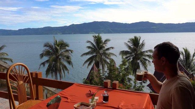 Young caucasian man drinking coffee at restaurant with Toba lake view