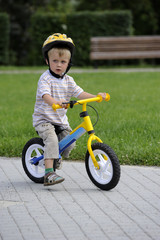 Child boy riding on his first bike with a helmet. Bike without pedals. Child learning to ride and balance on his two wheeler bike with no pedals.

