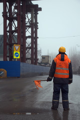 Worker in uniform with flag standing across the road preventing traffic in the construction area