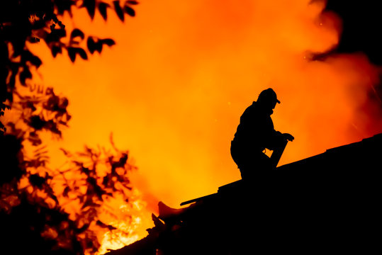 Silhouettes of firemen on the roof of a burning house