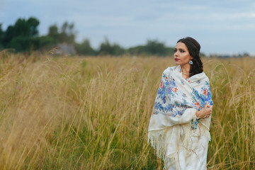 Young brunette wraps herself in a shawl standing on the field in