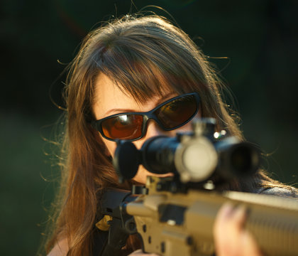 Girl with a gun for trap shooting and shooting glasses aiming at