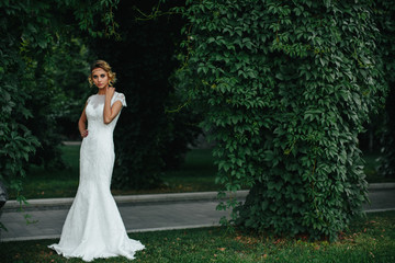 Model in a white maxi dress stands behind a pass in the park