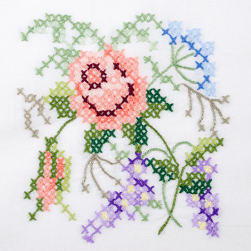 Flowers motif hand embroidery on white linen tablecloth.  Multicolored cross stich decoration with yarn. Handicraft. Macro photo close up from above.