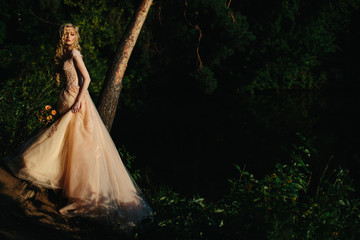 Gorgeous young blonde in logn evening dress in a forest