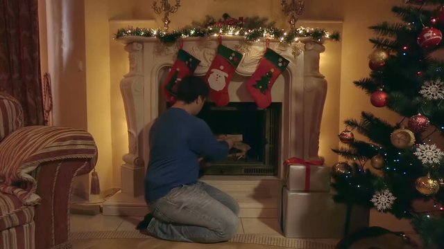 Young man inflaming fire in fireplace at living room decorated for Christmas