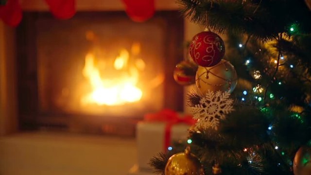 Background with colorful baubles on Christmas tree next to burning fireplace at living room