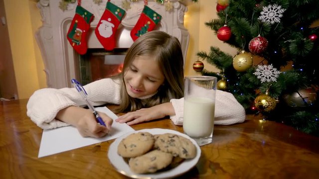 Dolly shot of cute girl writing letter to santa at living room with fireplace