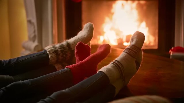 Closeup of family in woolen socks warming by the burning fireplace at house