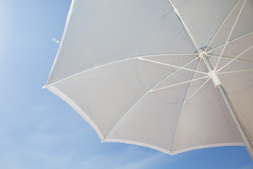 Under a grey beach umbrella looking up into the opened parasol against a blue sunny sky © OceanProd