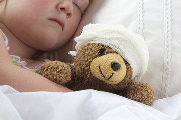 Girl in bed cuddling a teddy with bandage