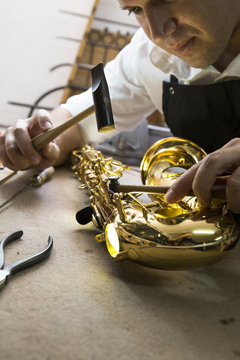 Instrument maker using a hammer repairing a saxophone
