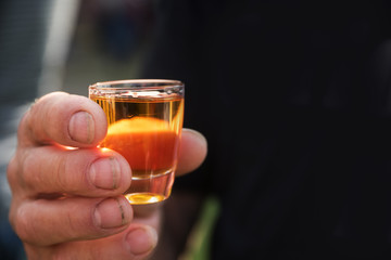 dirty mens hand holding a shot glass with a orange alcohol drink