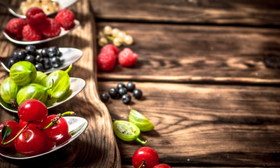 Different berries spoons. On wooden background.