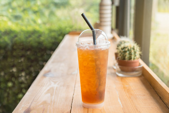 Iced lemon tea in a tall plastic cup on the wooden table. In homemade coffee shop.