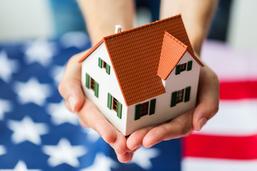 close up of hands holding house over american flag
