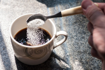 Serving sugar in coffee cup. Hand with teaspoon putting sugar in coffee cup. Sugar falling into cup...