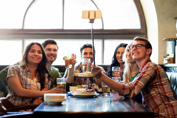 happy friends with selfie stick at bar or pub