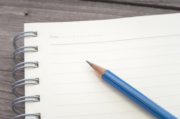 Notebook and pencil on wood background.