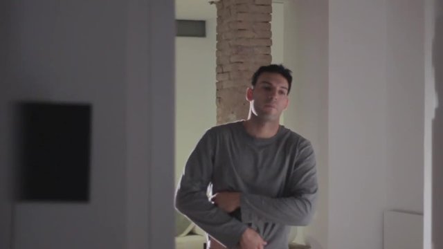 Handsome sexy young dark haired man with tattoo on left arm undressing from the waist up, slo-mo, MS