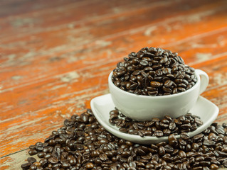 Coffee beans in a cup and spilling out of a cup, on Wooden table .
