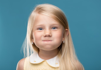Small, young, funny girl, inflated cheeks on blue background

