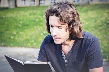 Young man resting and enjoying a book reading at the lawn in the park in peaceful atmosphere.