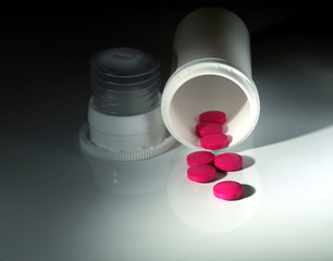 spilled red pills and white plastic bottle on white background under spot light, closeup