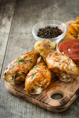 Roast chicken drumsticks and chips on wooden table

