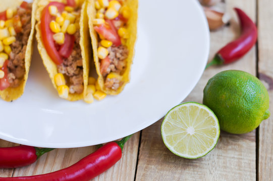 Cooked mexican tacos, red chili pepper and freshly sliced green lime on wooden background