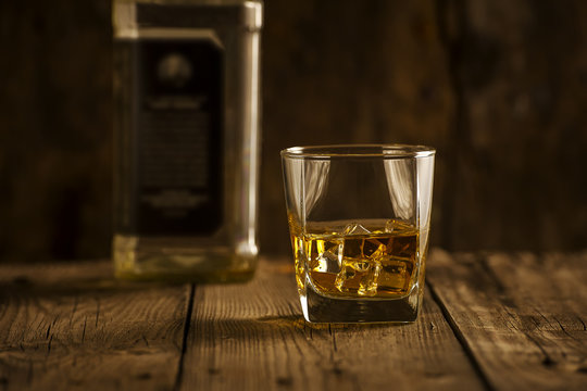 A Glass of whiskey and empty Bottle of whiskey on a wooden background