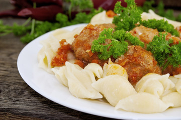 Pasta Conchiglie and meatballs with tomato sauce on rustic woode