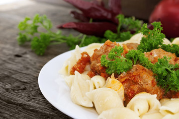 Pasta Conchiglie and meatballs with tomato sauce on rustic woode