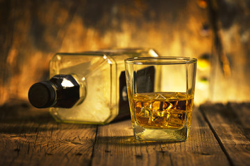 A Glass of whiskey and empty Bottle of whiskey on a wooden background