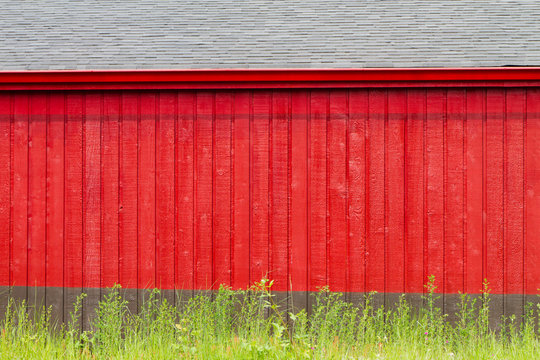 Rustic Vivid Red Vertical Wooden Plank and Gray Side of  Building Backdrop with Green Grass Border on Bottom of Frame. Copy space.