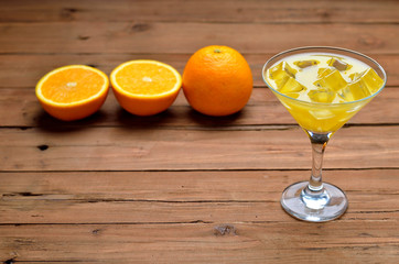 A glass of fresh orange juice with ice cubes on brown wooden bac