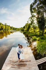 The bride and groom are standing on a wooden pier near the pond