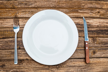 Empty plate, fork and knife on wooden background