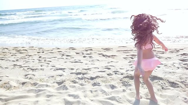 Slow motion of a cute little girl in swimsuit playing at the sea beach
