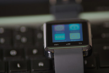 Smartwatch with screen lit up sitting on top of computer keyboard, very nice all black concept