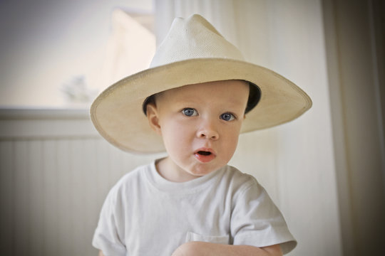 Young boy trying on a man's hat and looking at the camera
