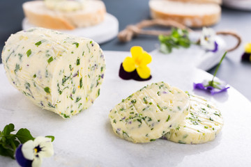 Herb butter with edible flowers on marble cutting board, healthy food.