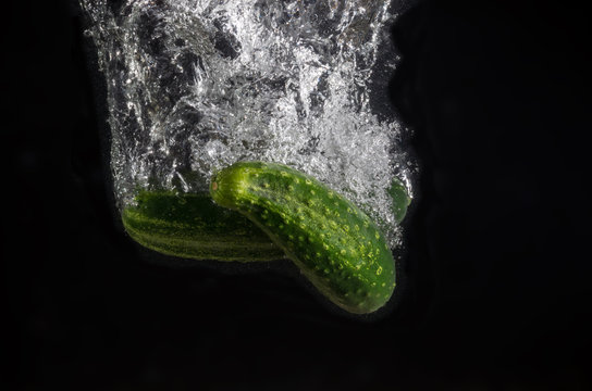 Two fresh cucumbers with water splash on black background