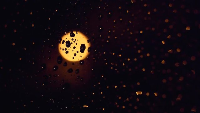 Abstract night city light over wet window with shining rain drops. Movement of the glass, smoth change of depth of field. Time lapse