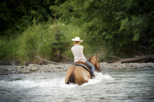 Mid-adult woman riding a horse through a river.
