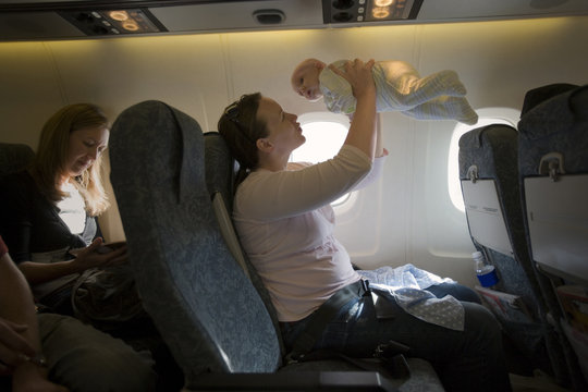 Young mother holding her young baby while sitting inside a plane.