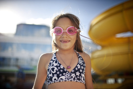 Young girl with missing teeth wearing swimming goggles at a swmming pool.