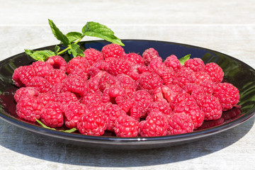 Red raspberries on a black plate on gray wooden background
