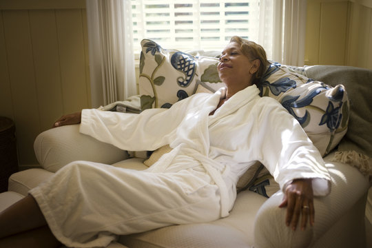 Mid-adult woman lounging on a couch wearing a bathrobe.